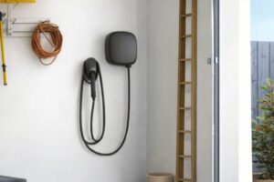 En modern svart elbilsladdare monterad på en vit garagevägg.