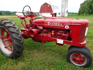 En klassisk röd veterantraktor av märket Farmall på en gräsmatta framför en lada.