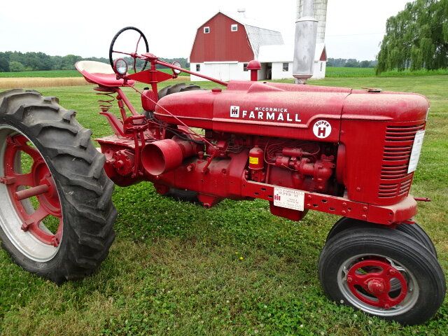 En klassisk röd veterantraktor av märket Farmall på en gräsmatta framför en lada.